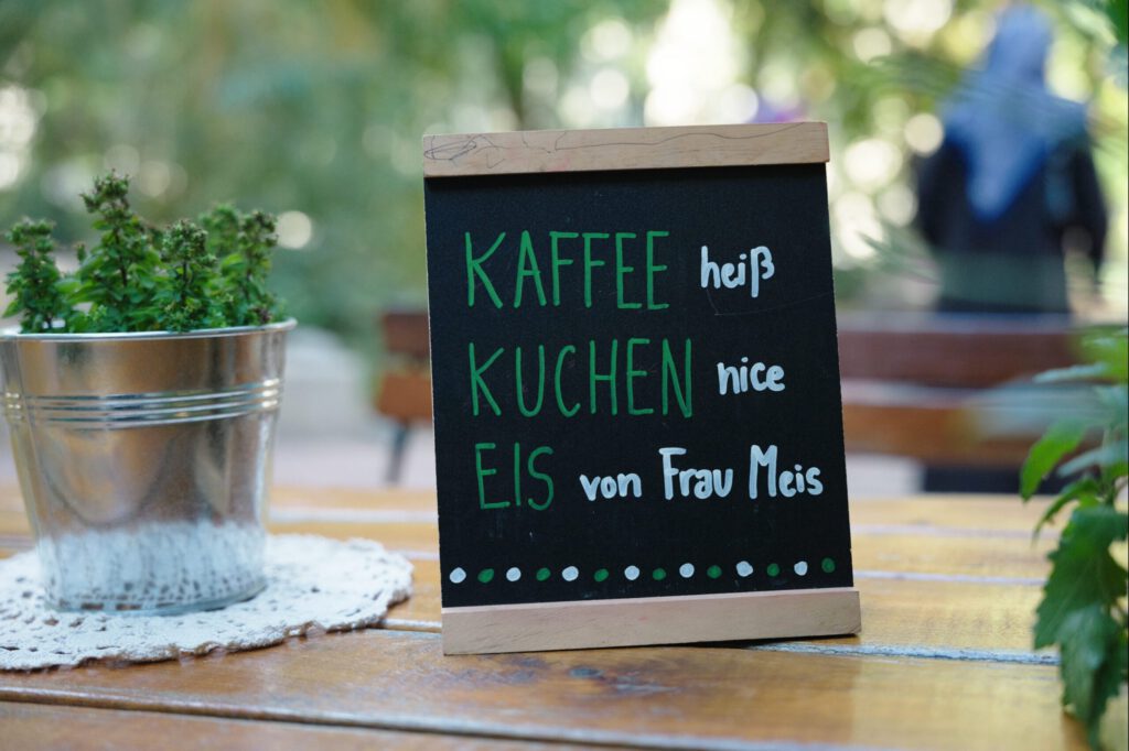 Schild mit der Aufschrift Kaffe heiß, Kuchen nice, Eis von Frau Meis"