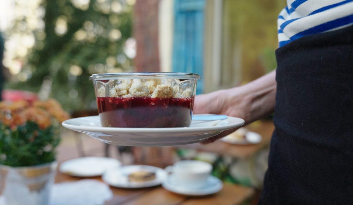 Eine Hand hält von rechts ein Glas mit Fruchtcrumble ins Bild