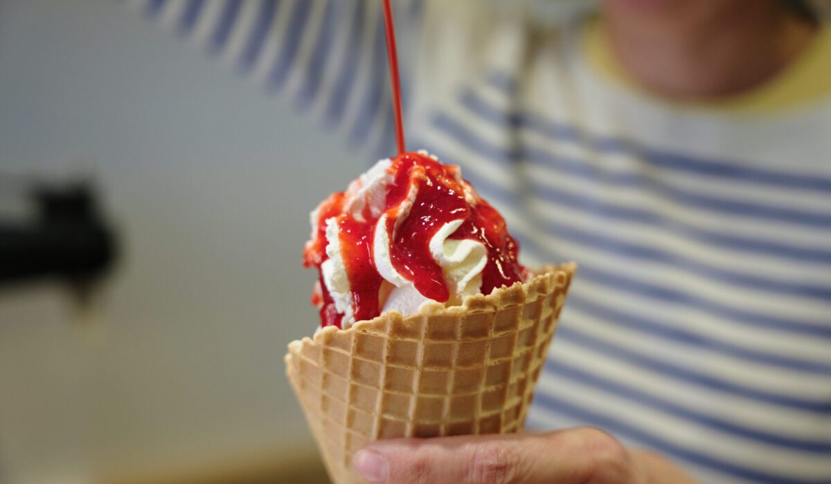 Ein Eis mit Sahne in der Waffel, von oben fließt Erdbeersauce auf die Sahne