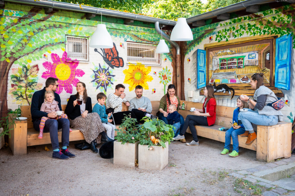 Mehrere Personen mit Kindern sitzen auf einer Holzbank vor – Frau Meis Eis · Café
