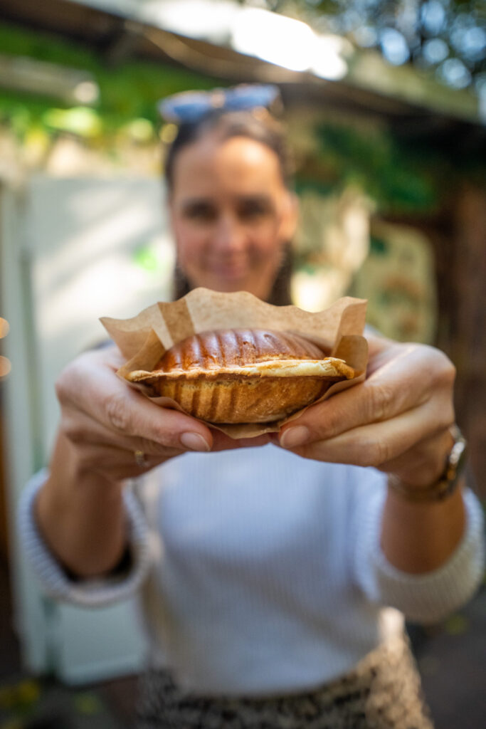 Eine Frau hält einem eine Brioche im Backpapier entgegen