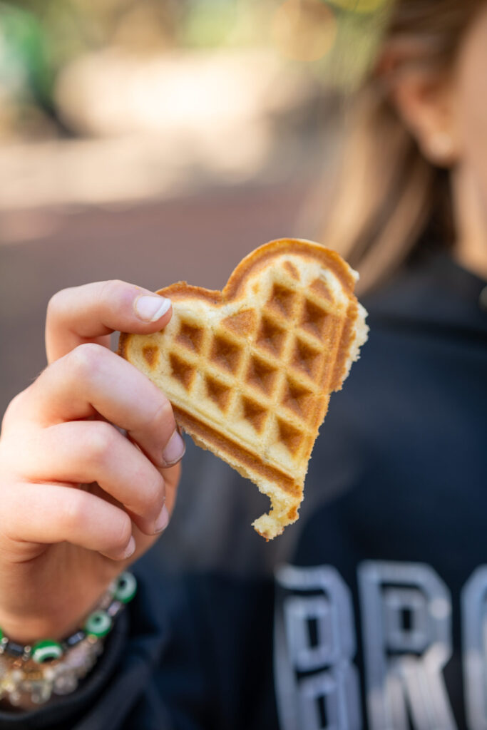 Kind hält ein Stück einer herzförmigen Waffel
