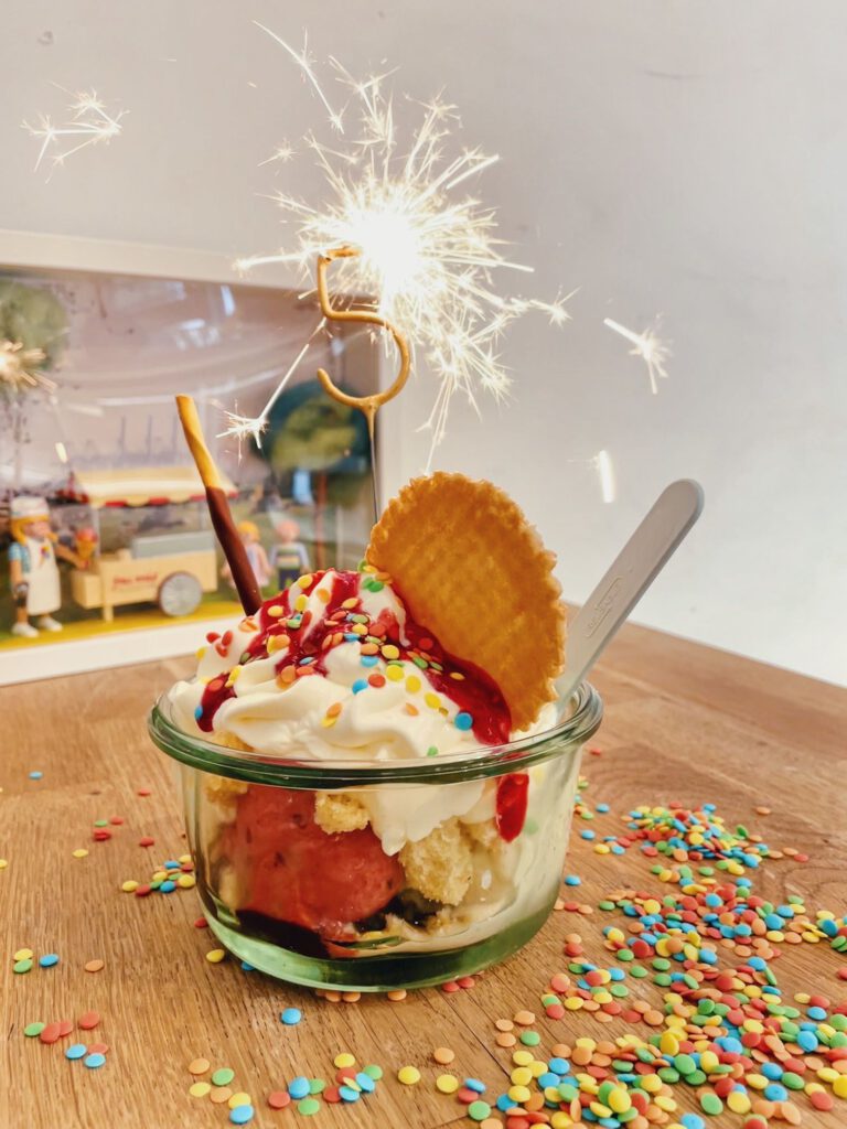 Eisbecher mit einer Wunderkeze in Form einer 5, Waffeln, Sahne und bunten Streuseln